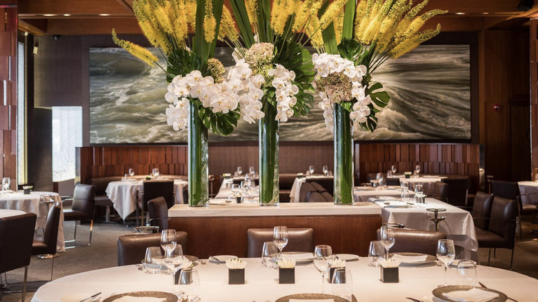 Tables with white linens and three towering floral arrangements in the center of a dining room