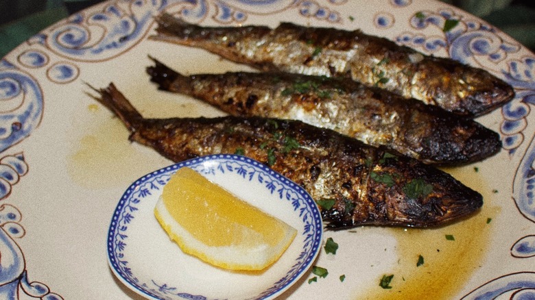 Grilled sardines on a plate with lemon wedge
