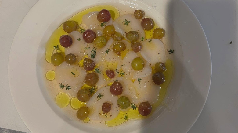 Crudo with grapes and olive oil on white plate