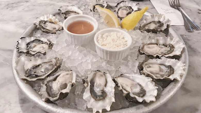 Platter of raw oysters on ice with condiments in the middle
