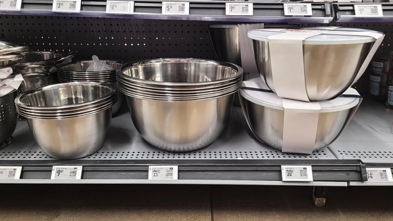 Different stacks and sets of metal mixing bowls on a shelf.