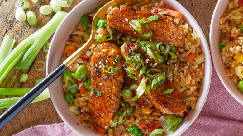 Bowl of rice topped with glazed and cooked tempeh, spring onions, and vegetables