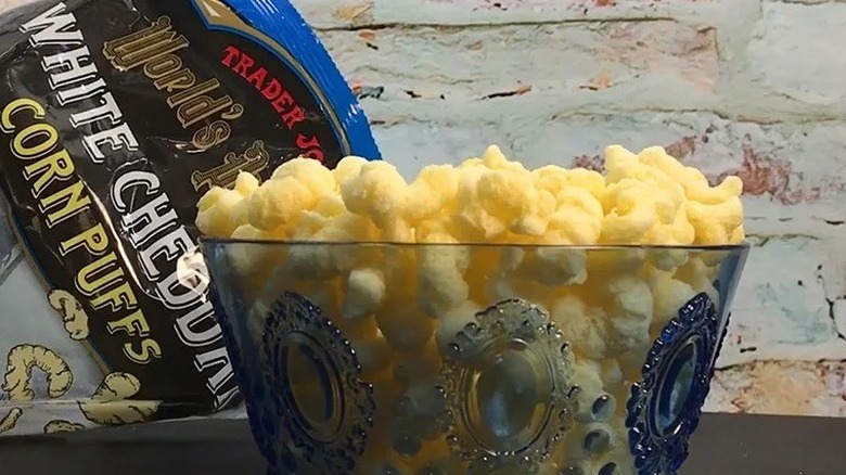 Bowl of world's puffiest white cheddar corn puffs in front of plastic packaging on table