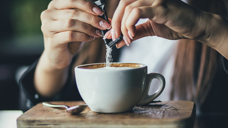 Person pouring sugar into coffee