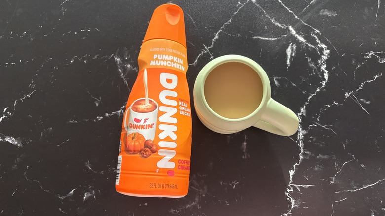 Dunkin' pumpkin munchkin coffee creamer bottle next to cup of coffee