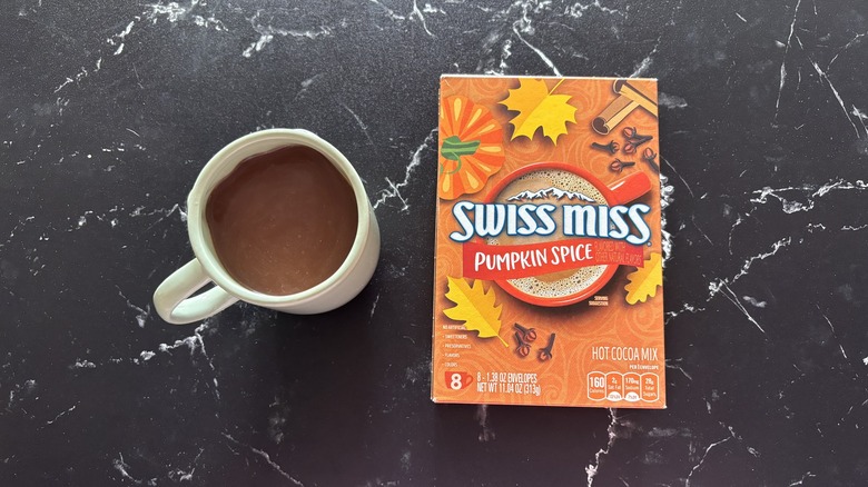 Swiss Miss pumpkin spice hot cocoa mix box next to mug of hot cocoa