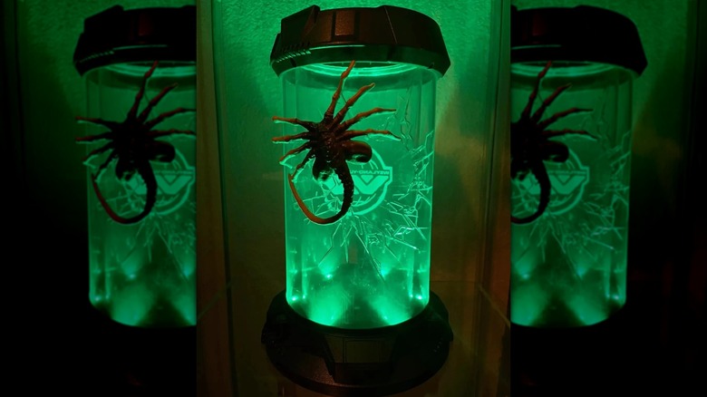 The glowing Alien: Romulus facehugger popcorn bucket glowing green in a dark room