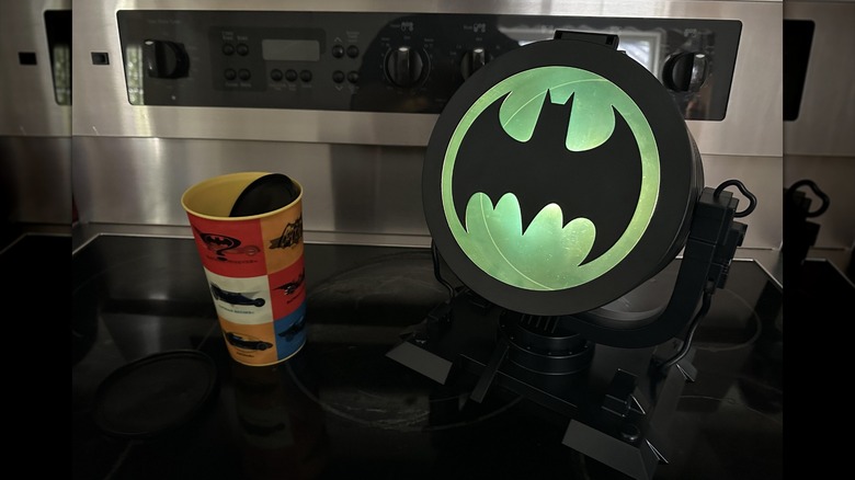 The Batman Bat Signal popcorn bucket sits on a table next to a soda cup.