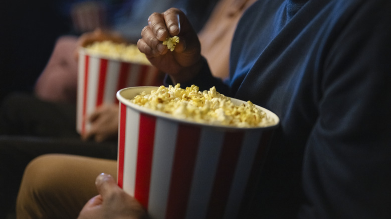 people sitting in movie theater eating popcorn out of buckets