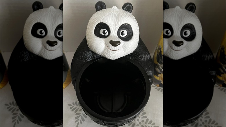 A popcorn bucket shaped like a panda bear holding a bucket sitting on a table