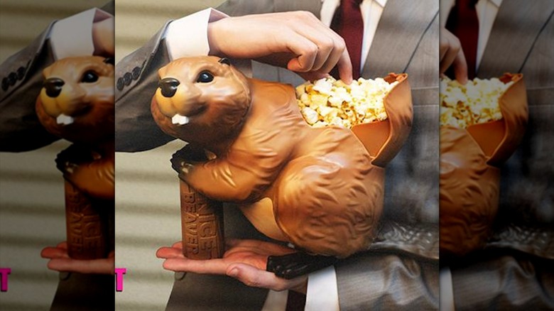 A man in a suit holds the Naked Gun beaver popcorn bucket