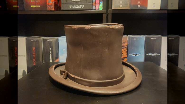 The Wonka hat popcorn bucket sits on a table in front of a shelf of movies