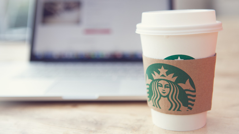 To-go cup of Starbucks coffee on table in front of a laptop computer