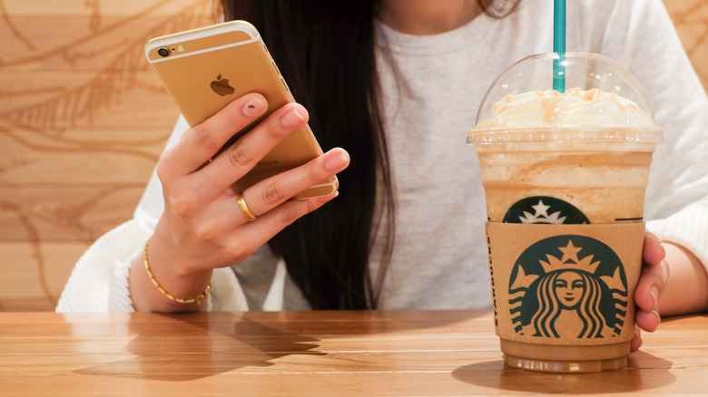 Person looking at phone while holding Starbucks Iced Caramel Macchiato