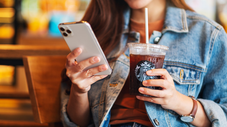 Person looking at phone while drinking Starbucks iced coffee