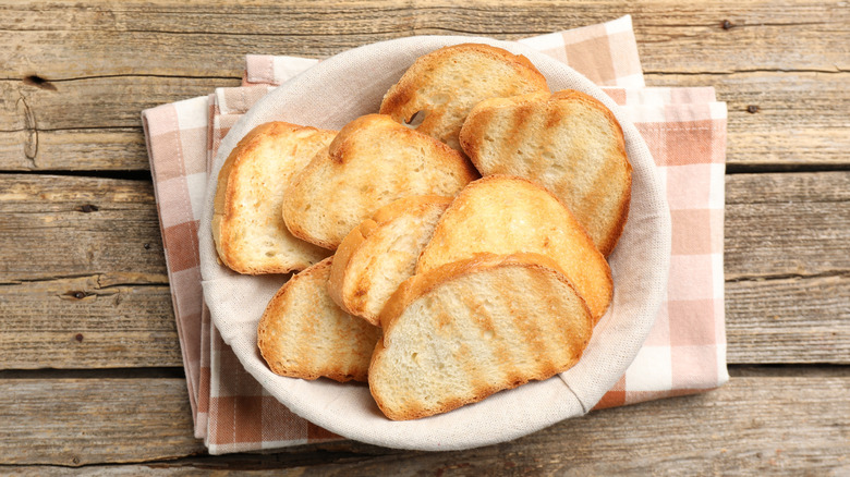 Basket of toasted bread sitting atop a folded tea towel on a wooden table