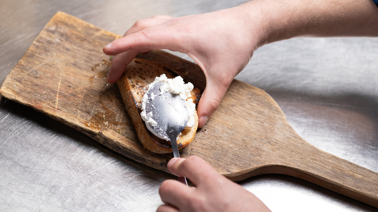 Person spreading cream cheese onto a slice of bread with a spoon