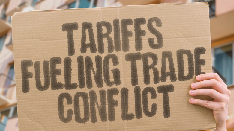 Person holding cardboard sign up displaying how tariffs are fueling trade conflict