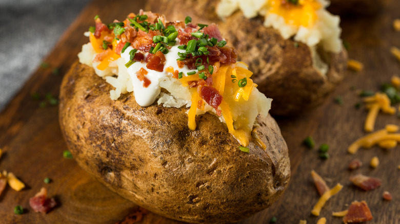 A loaded baked potato sitting on a cutting board topped with sour cream, bacon bits, and chives