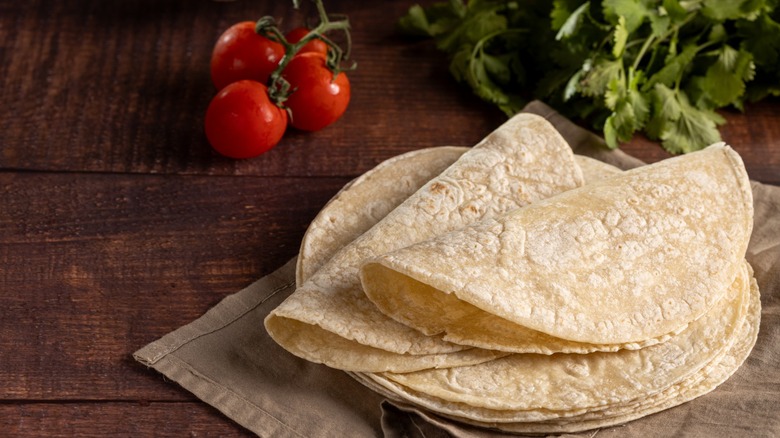 a stack of fresh, folded tortillas on a table with some tomato and cilantro