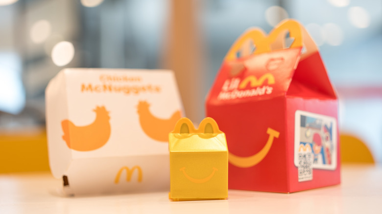 Someone in a car grabbing a McDonald's Happy Meal box through the drive-thru window