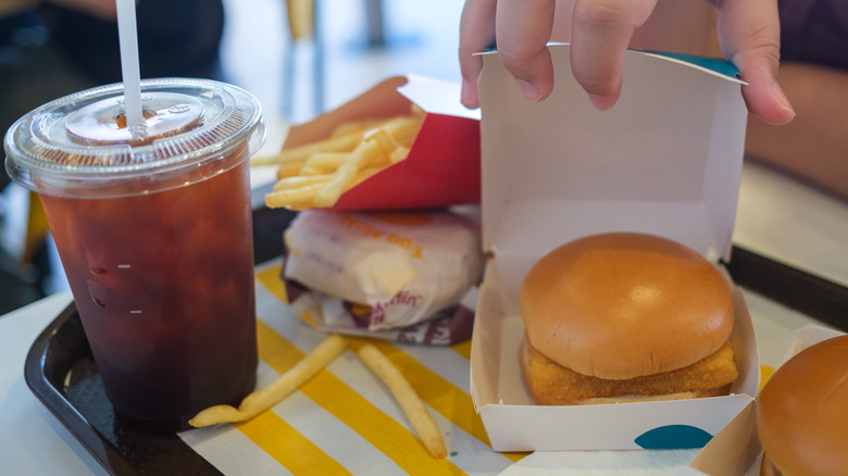 Hand holding open a Filet-O-Fish box on a McDonald's tray beside fries, a drink, and other sandwiches