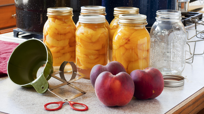 Jars of peaches next to peach canning supplies on a kitchen counter