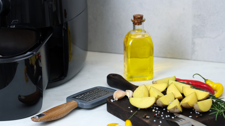 A chopping board of potatoes next to oil and spices and an air fryer