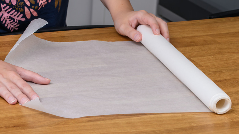 woman unrolling parchment paper on kitchen counter