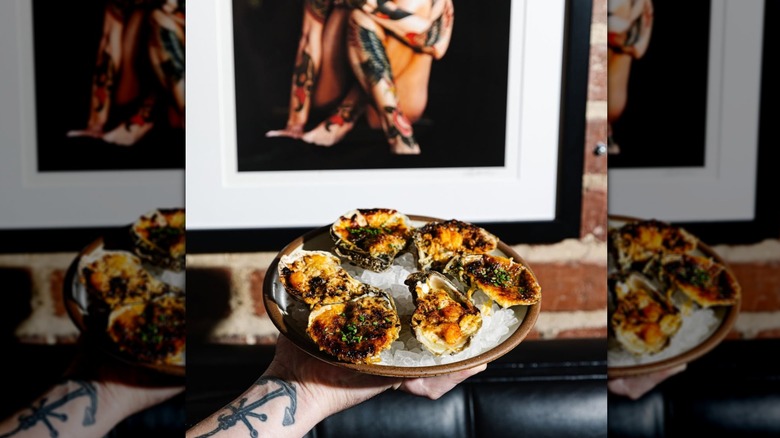A person holding a plate of oysters on ice with orange toppings