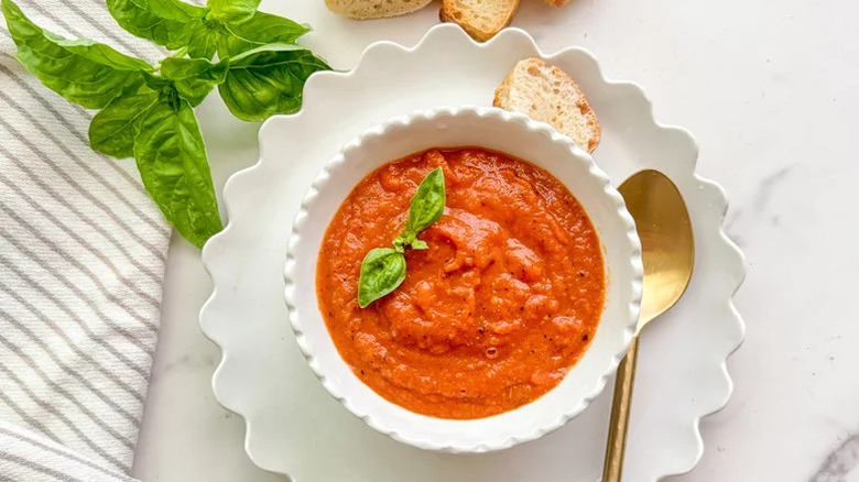 Tomato soup in white bowl with sprig of basil