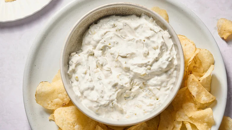 Onion dip in white bowl on white plate with potato chips