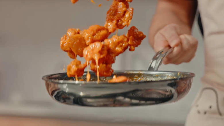 Someone tossing orange chicken in a pan