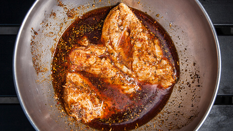 Chicken breasts marinating in a dark sauce inside a metal bowl.
