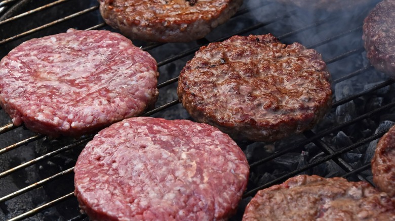 raw and browned hamburgers cooking on a grill