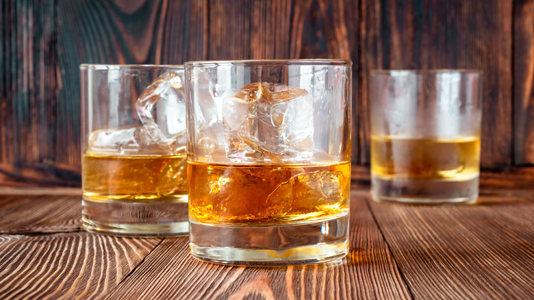 Three glasses of bourbon with ice sit on a wooden table