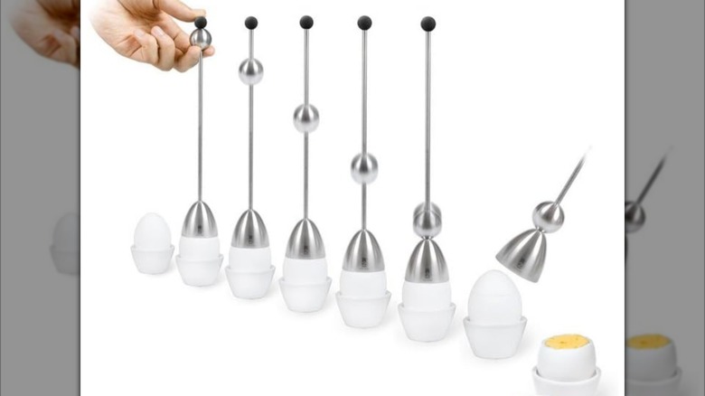 Hand using one of multiple egg crackers on line of eggs