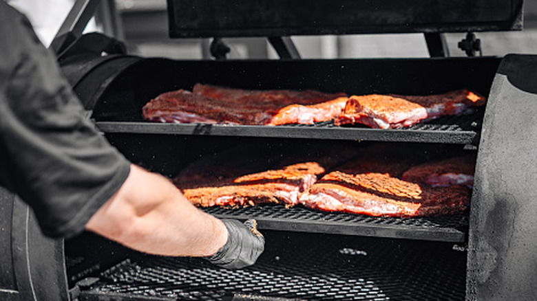 A person operating a smoker with racks of brisket
