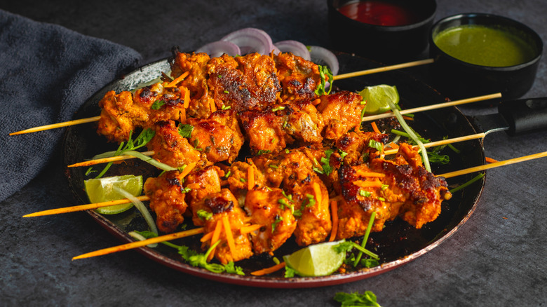 chicken tikka skewers on a plate with lime wedges and bowls of chutney