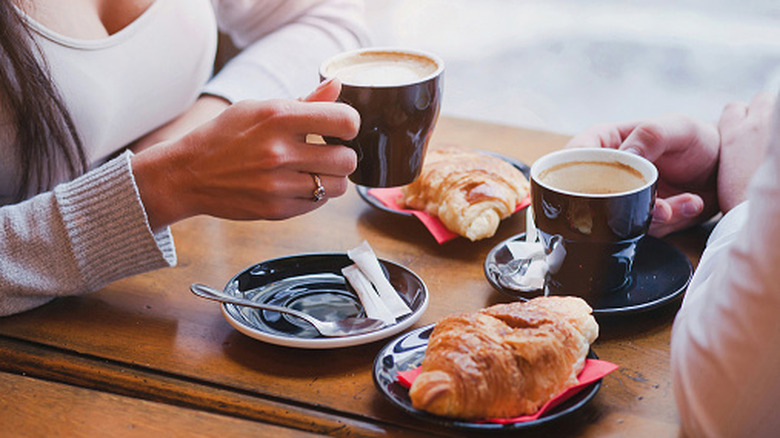 two people drinking coffee and eating croissants