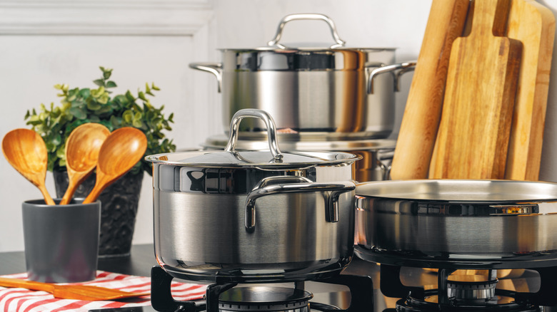 A collection of cookware on a stove top next to cooking utensils
