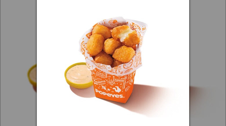 Popeyes Cheese Bites inside orange cardboard box next to yellow cup of dipping sauce