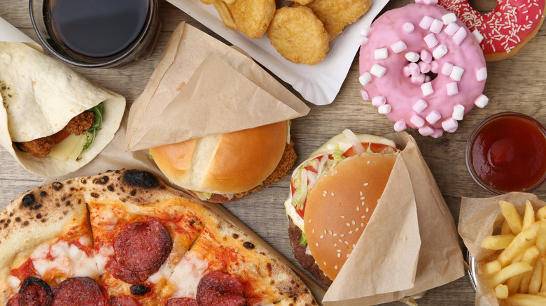 Pizzas, burgers, donuts, tacos, fries, nuggets and drinks on a table