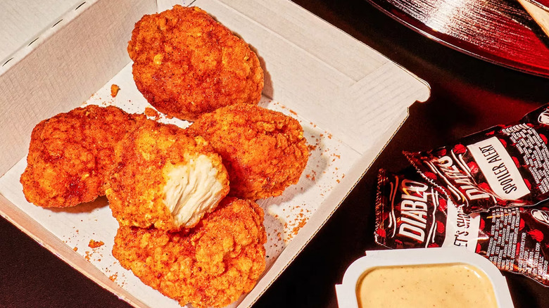 A box of Diablo Dusted Crispy Chicken Nuggets on a table next to a variety of Diablo sauces