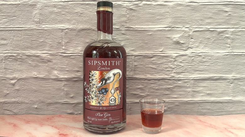 Bottle and shot glass of Sipsmith sloe gin on pink table