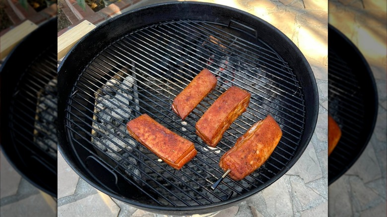 Pork belly slabs on a grill with pecan wood chunks