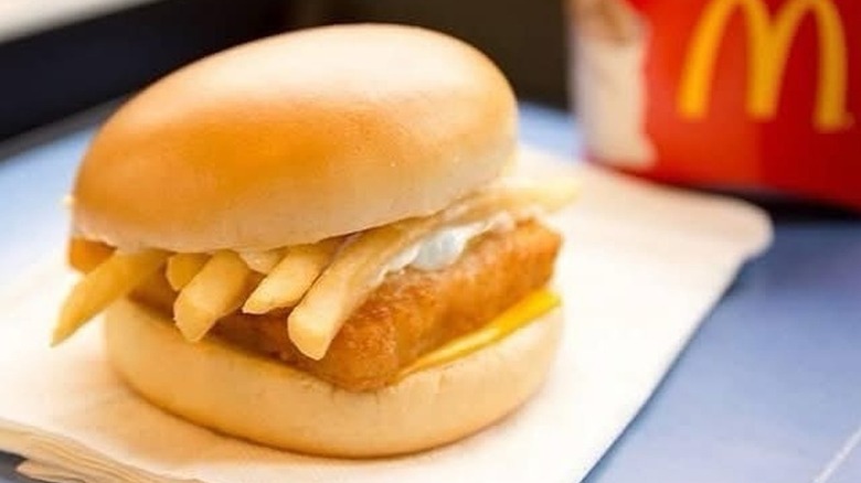 A Filet-O-Fish sandwich topped with french fries sitting on a napkin