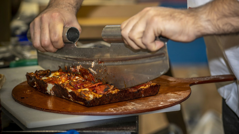 Chef slicing a Detroit-style pizza on wood cutting board