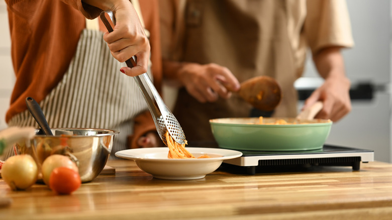 Couple cooking and plating spaghetti at counter