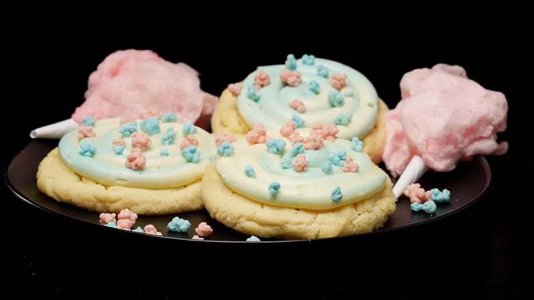 A plate of cotton candy-flavored cookies sit next to clouds of pink cotton candy on a black dish
